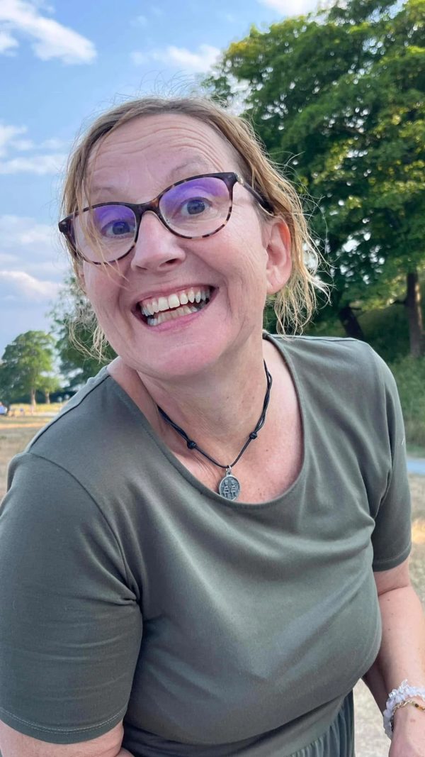 Birgitte smiler bredt med briller og grøn T-shirt, udenfor en sommeraften