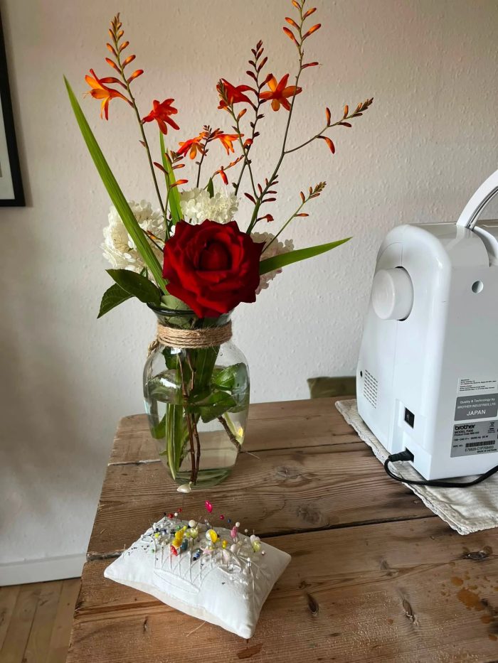 Værkstedet med symaskine, nålepude og en buket blomster på et træbord